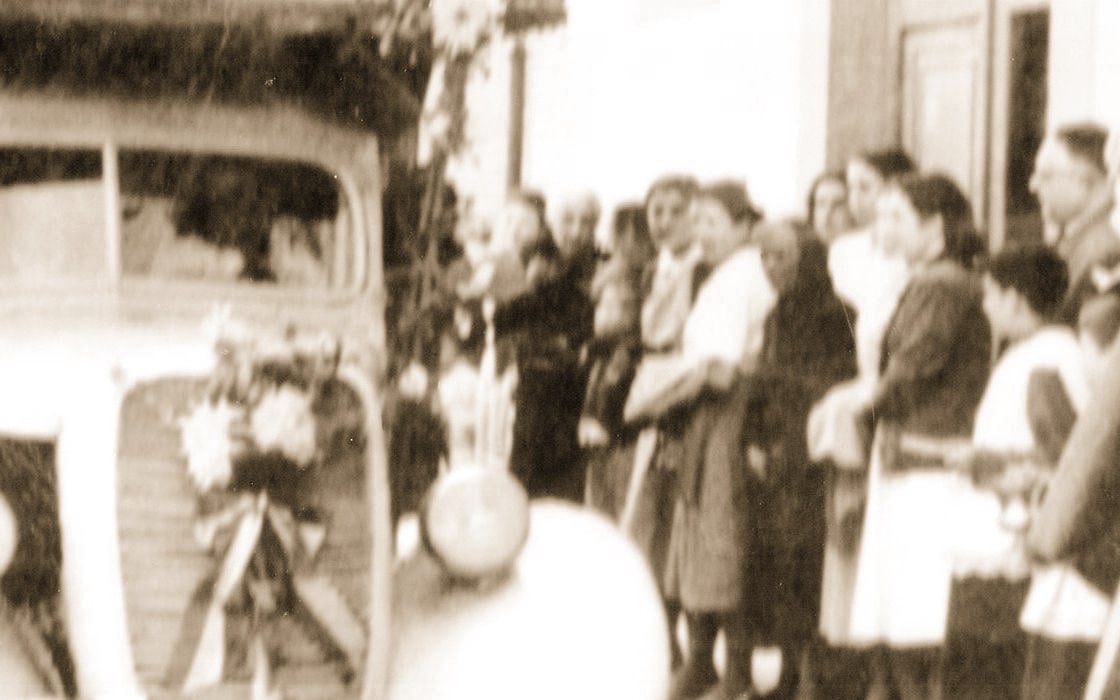 1950s photograph: a group of people beside an old vehicle decorated with flowers